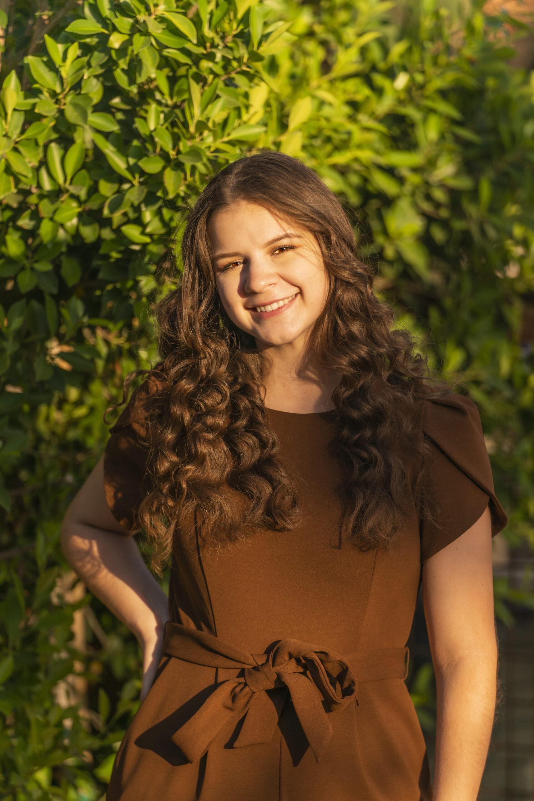 A woman with curly hair stands with her hand on her hip and smiles at the camera.