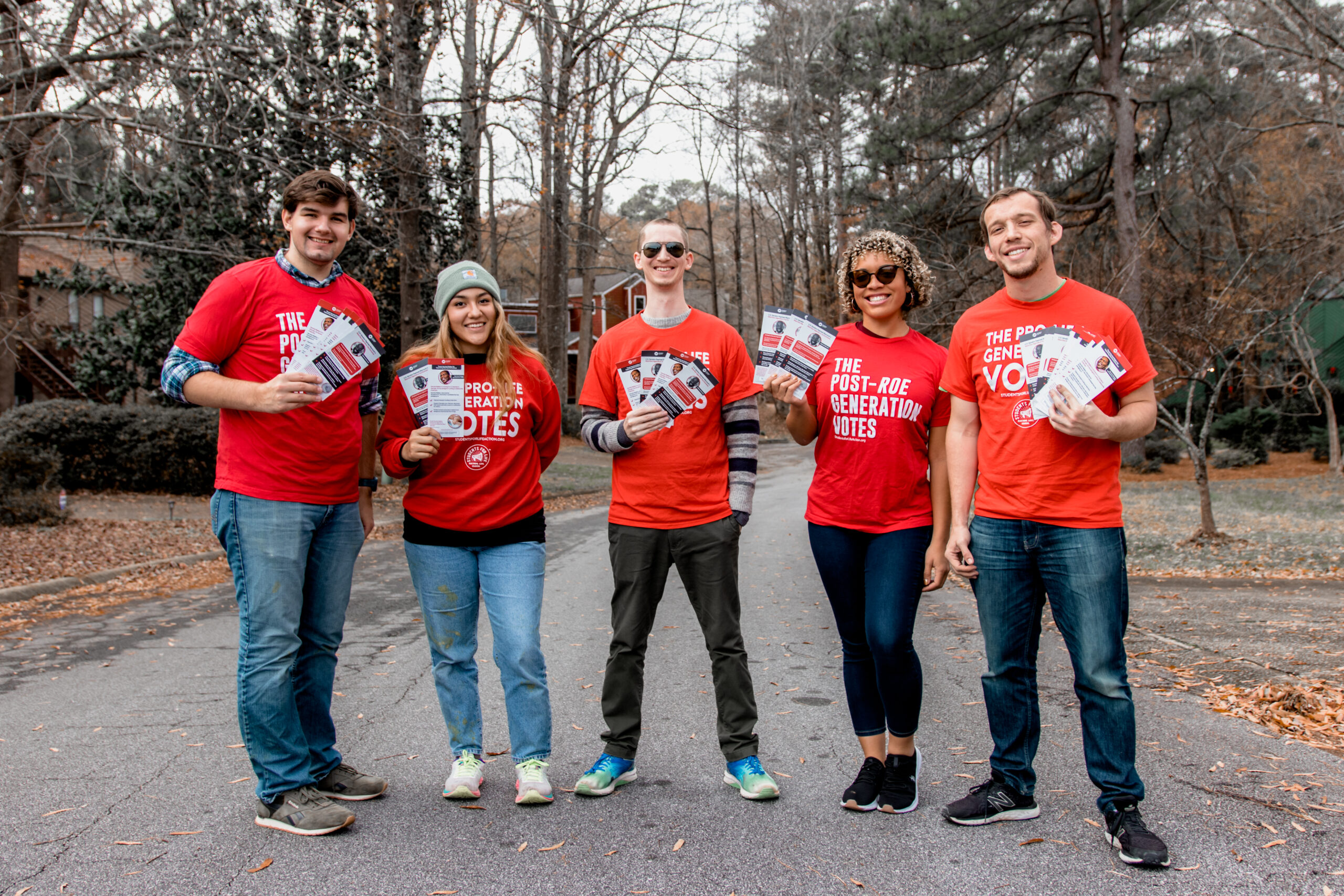 A group of people all wear the same shirt and pose for a photo with a wooded background.