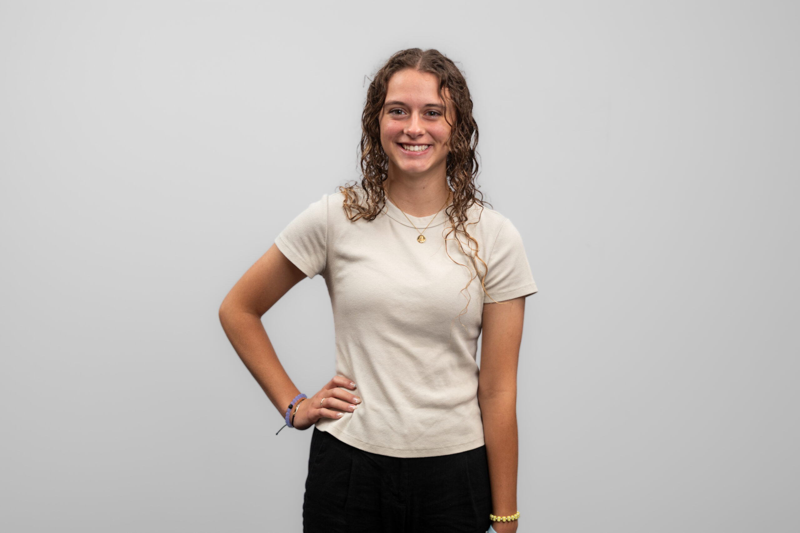 A woman wearing a white shirt stands with her hand on her hip and smiles at the camera.