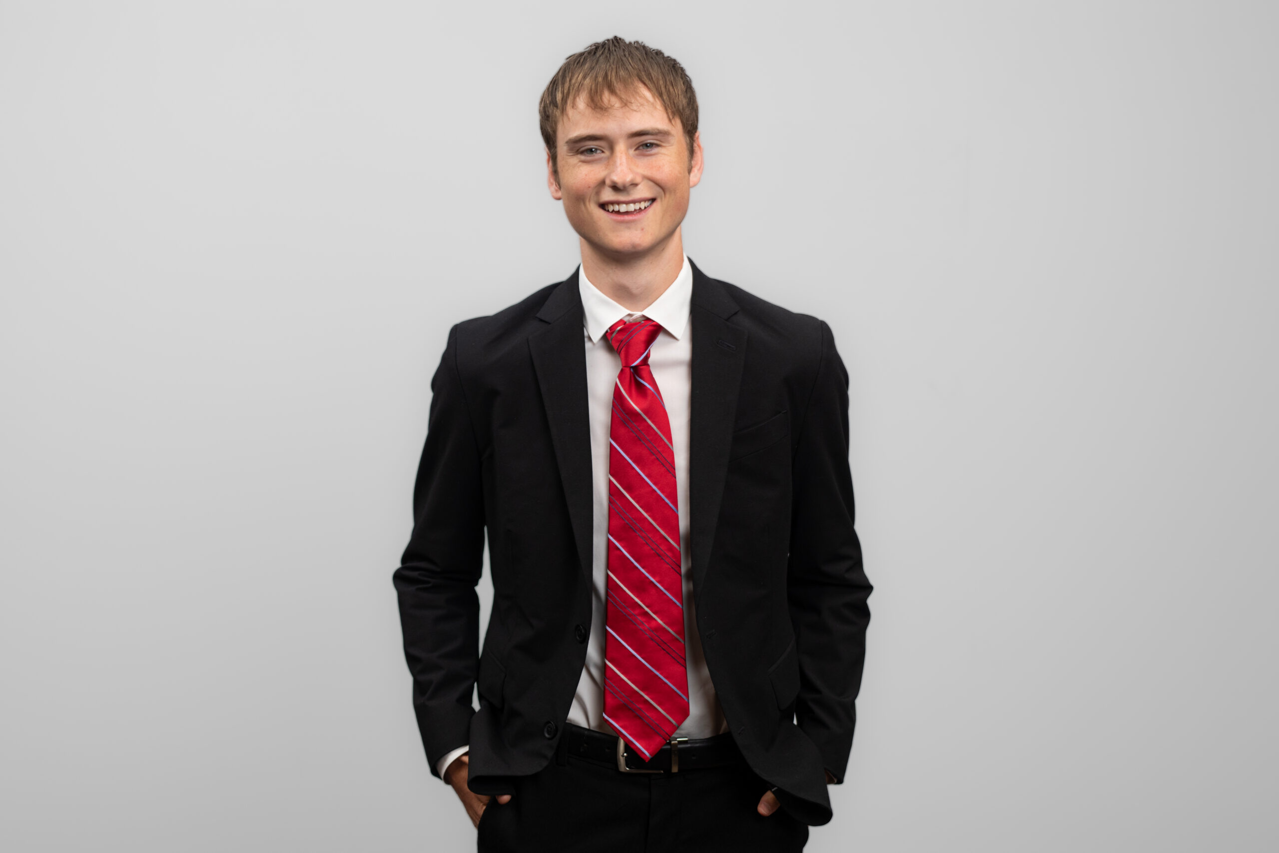 A man in a suit smiles while keeping his hands in his pockets.