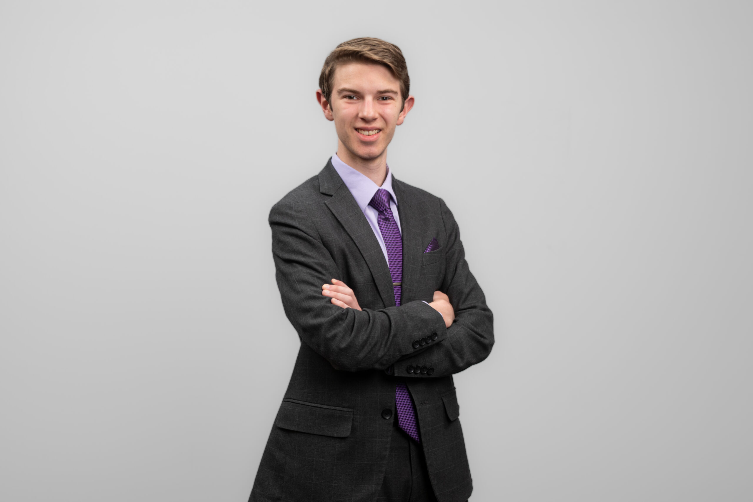 A man in a suit is turned slightly to the side. He is crossing his arms and smiling at the camera.