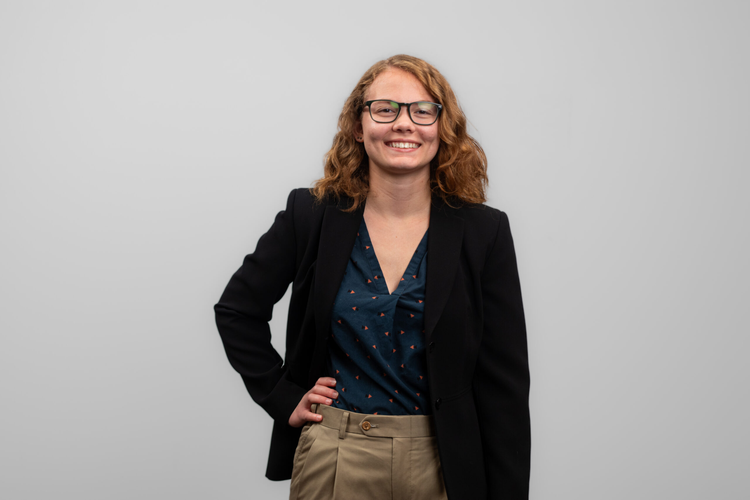A woman wearing glasses stands with her hand on her hip and smiles at the camera.