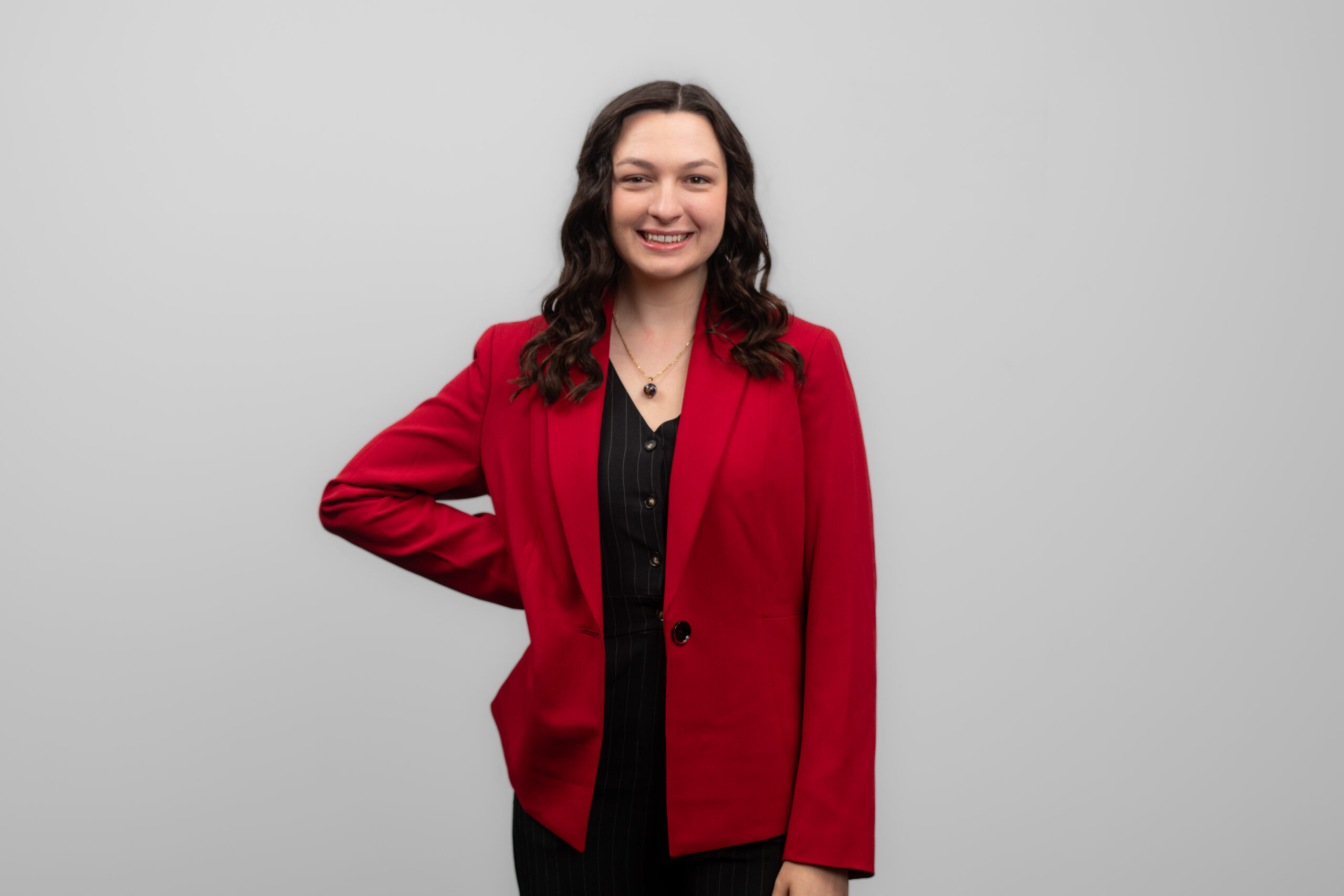 A woman with dark hair stands with her hand on her hip and smiles at the camera.