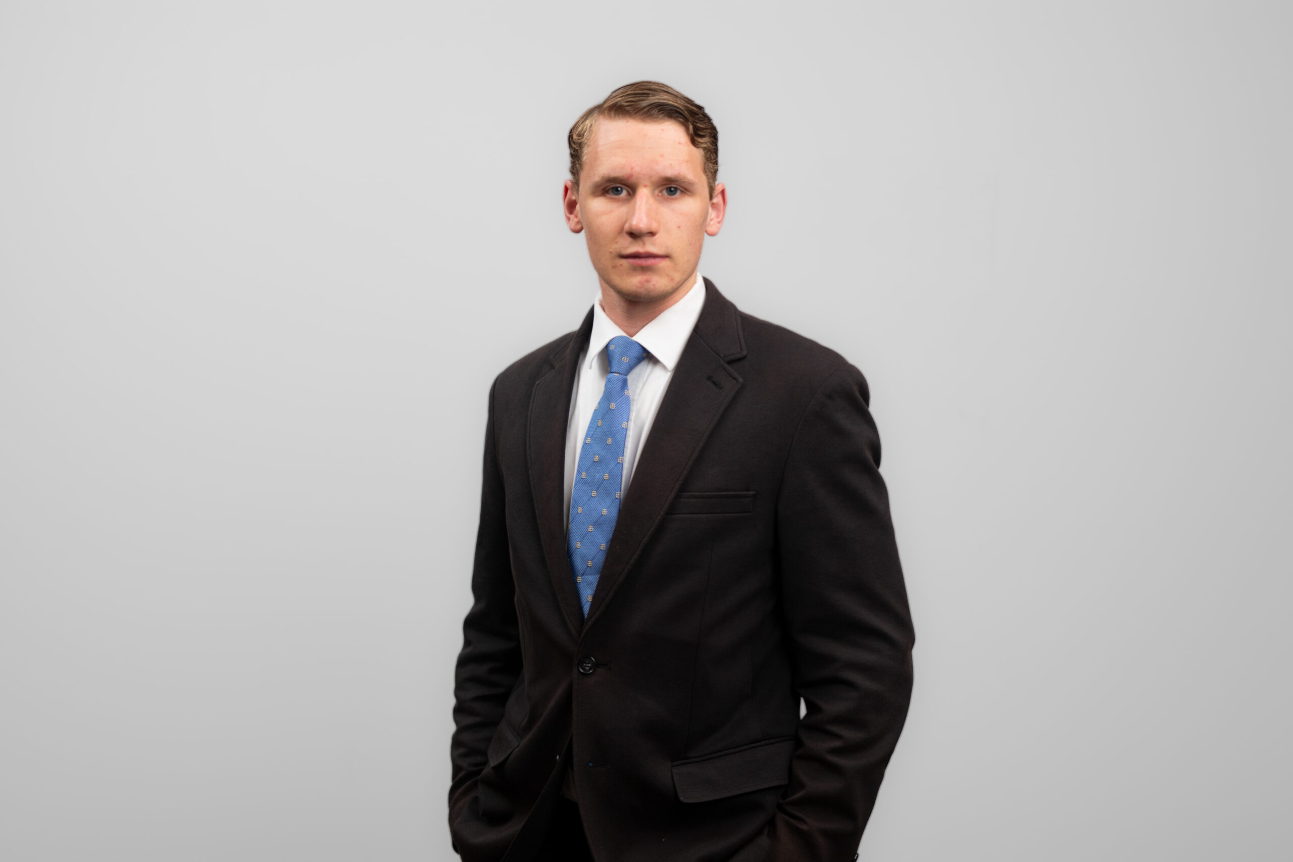 A man in a suit turns slightly to the side while looking at the camera.